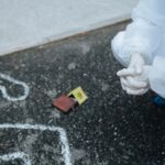 Technik kryminalistyki w kombinezonie bada kontur ofiary na asfalcie