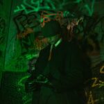 Mężczyzna w prochowcu i kapeluszu na tle kolorowego graffiti