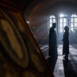 Sylwetki księdza i parafianki rozmawiających w jasnym wnętrzu kościoła