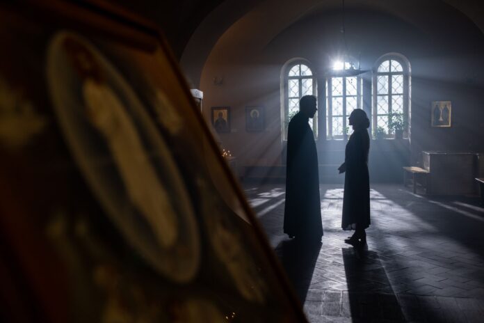 Sylwetki księdza i parafianki rozmawiających w jasnym wnętrzu kościoła