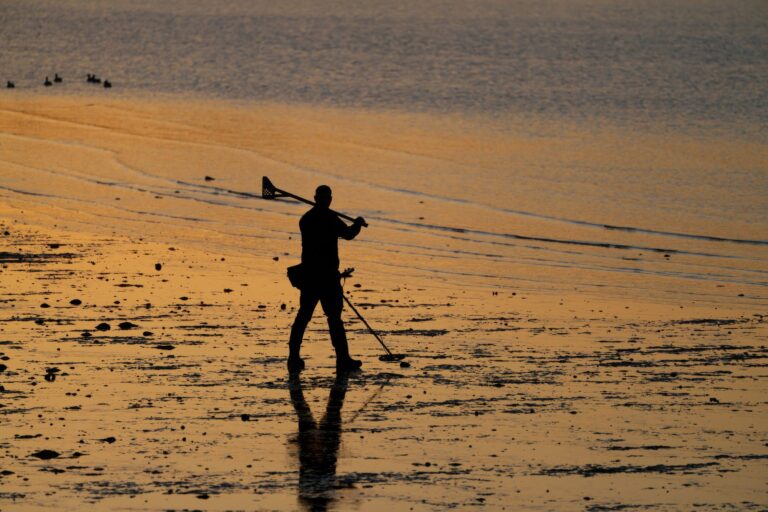 Sylwetka mężczyzny z wykrywaczem metalu na plaży o zachodzie słońca